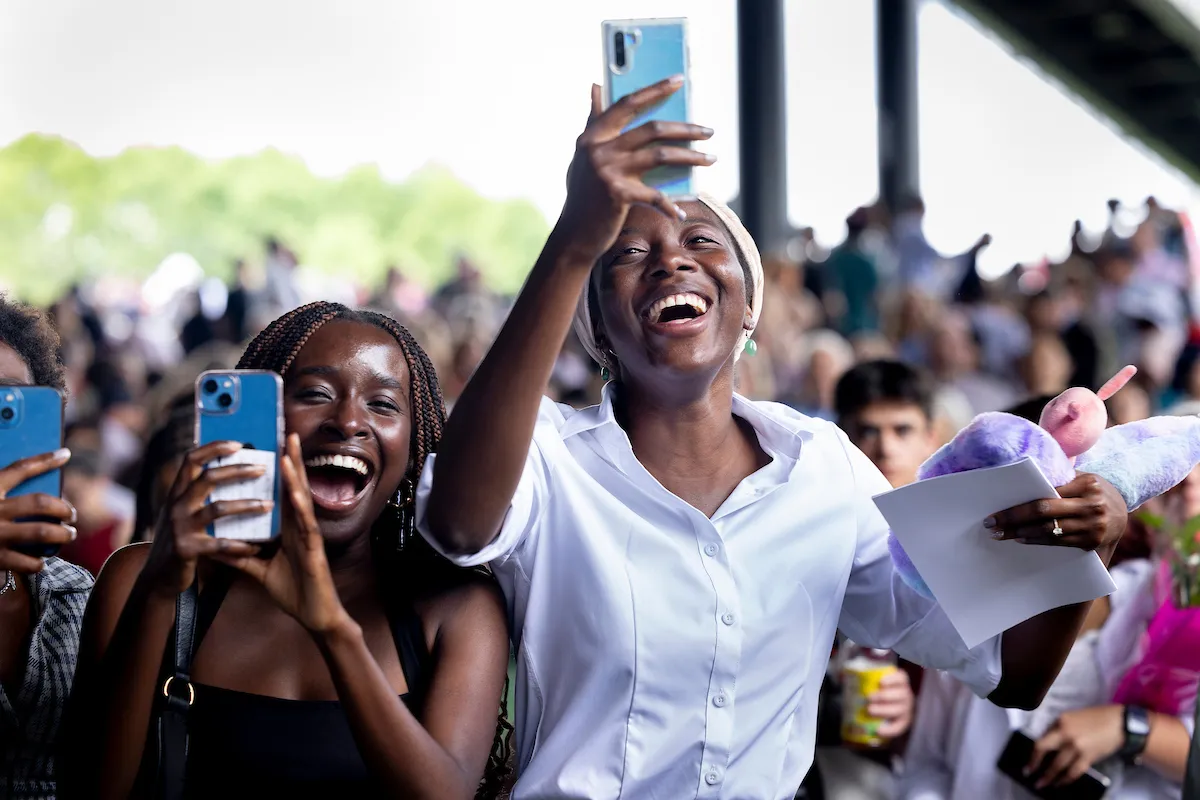 Smiling people take cell phone photos at commencement ceremony at Mann Center