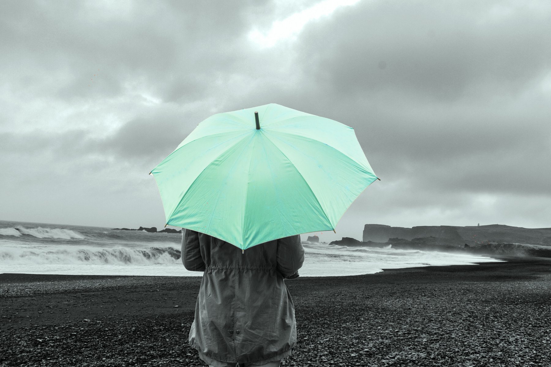A woman with an umbrella stands by the ocean. 