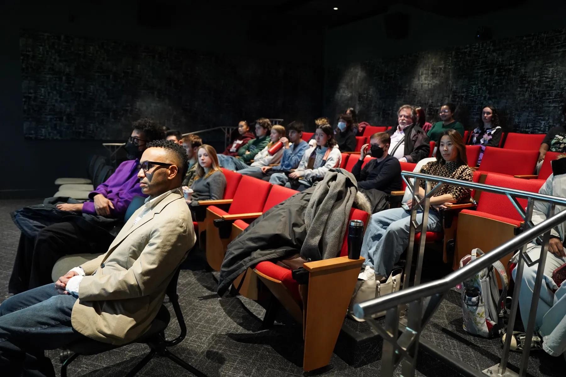 Students, faculty, and staff in the audience of the Ping and Rose Chen screening room sit in the screening room's cushioned red chairs