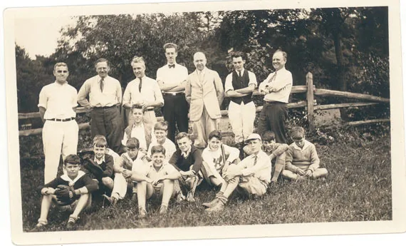 Photograph of a group of boys and men posing in front of a fence.
