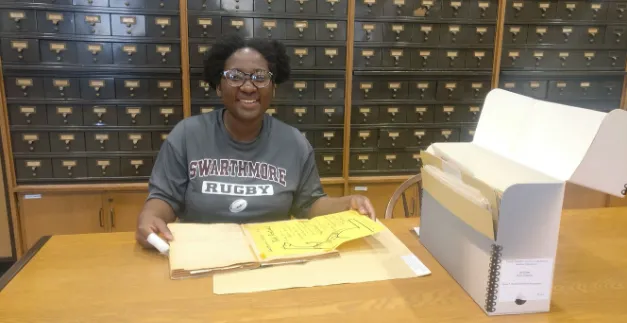 Student smiling in front of an open folder of archival documents