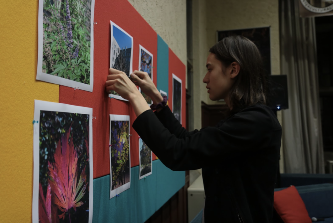 Student with long hair hanging photo on colorful bulletin board indoors