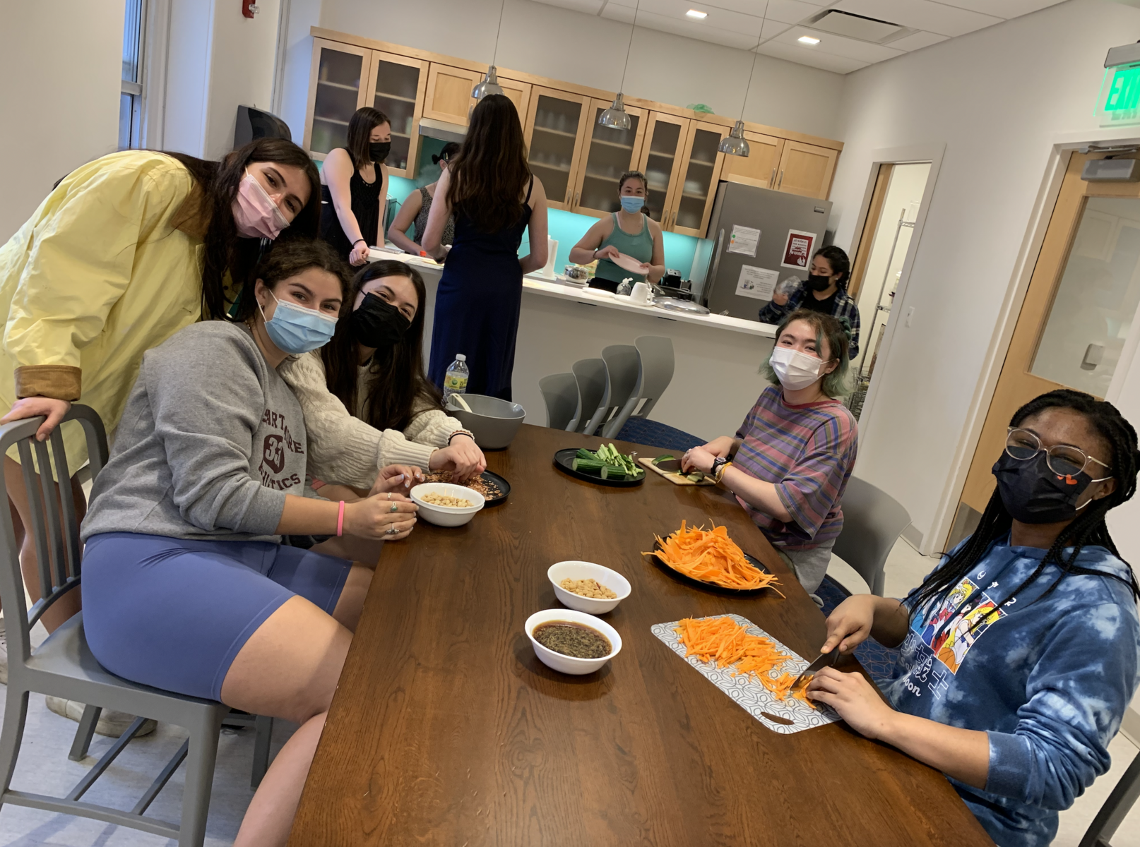 Masked students sitting around a table, prepping different ingredients to make a Vietnamese vermicelli bowl.