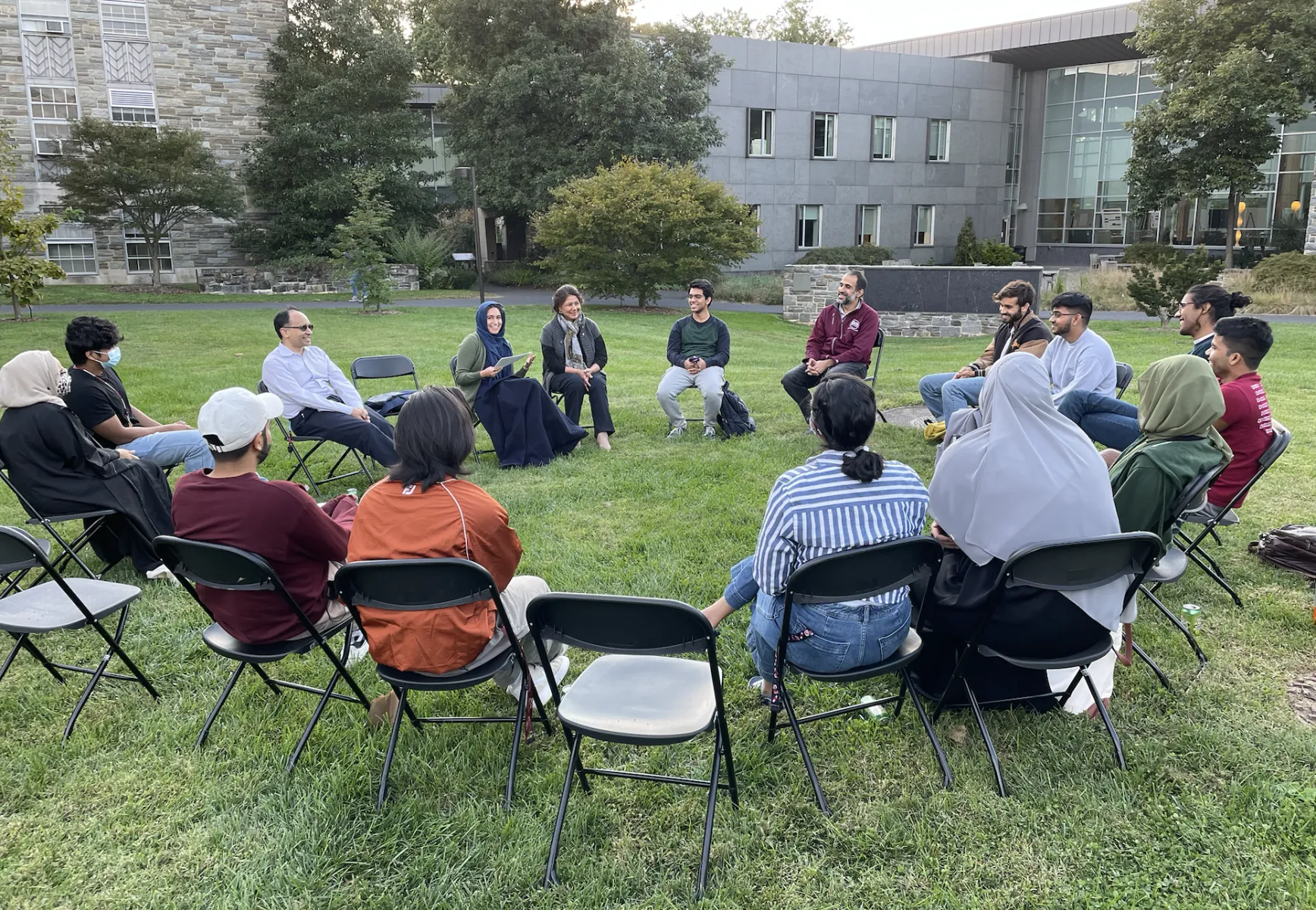 people sitting in chairs outside in a circle, smiling and talking