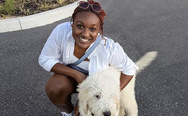 Gabriella Nash outdoors and kneeling near her white dog