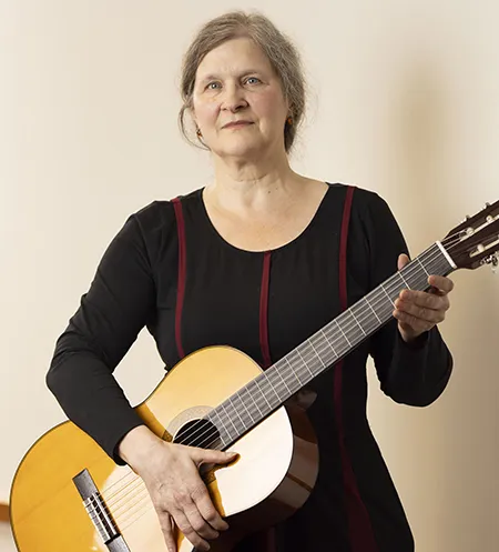 Professor Sibelan Forrester wearing a black dress and holding a guitar