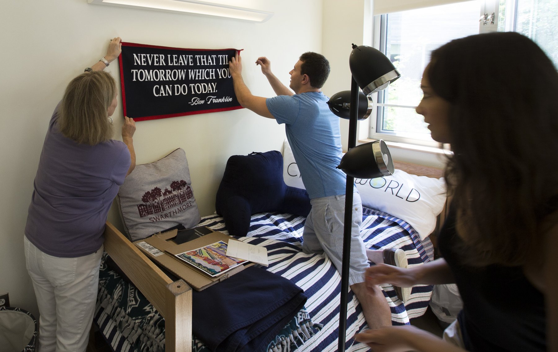 Student and parent hang decorative sign above the student's bed in a residence hall room. 
