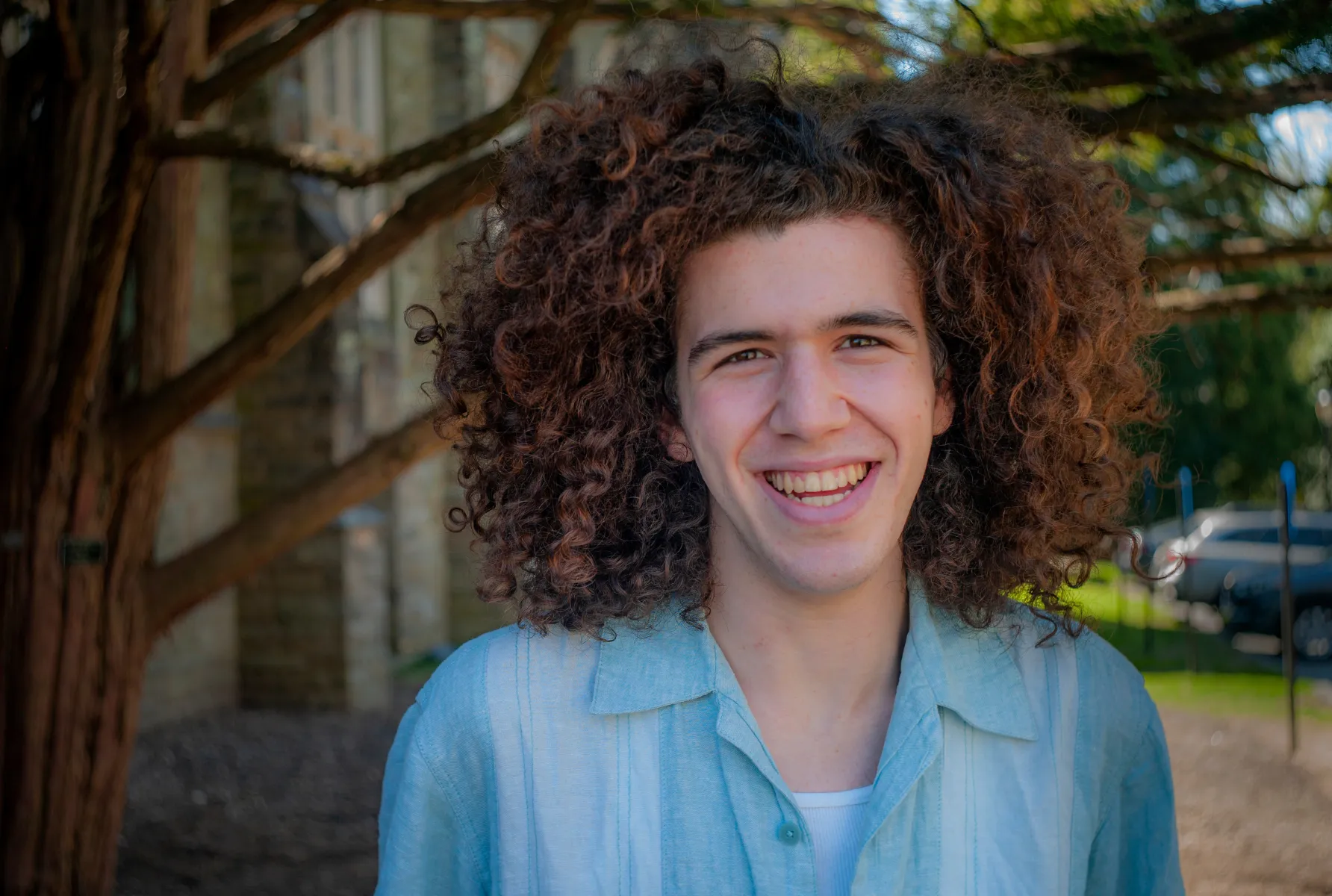 Student with curly hair stands in front of tree outdoors