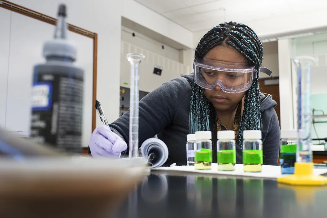 Student in chemistry lab with vials of green liquid