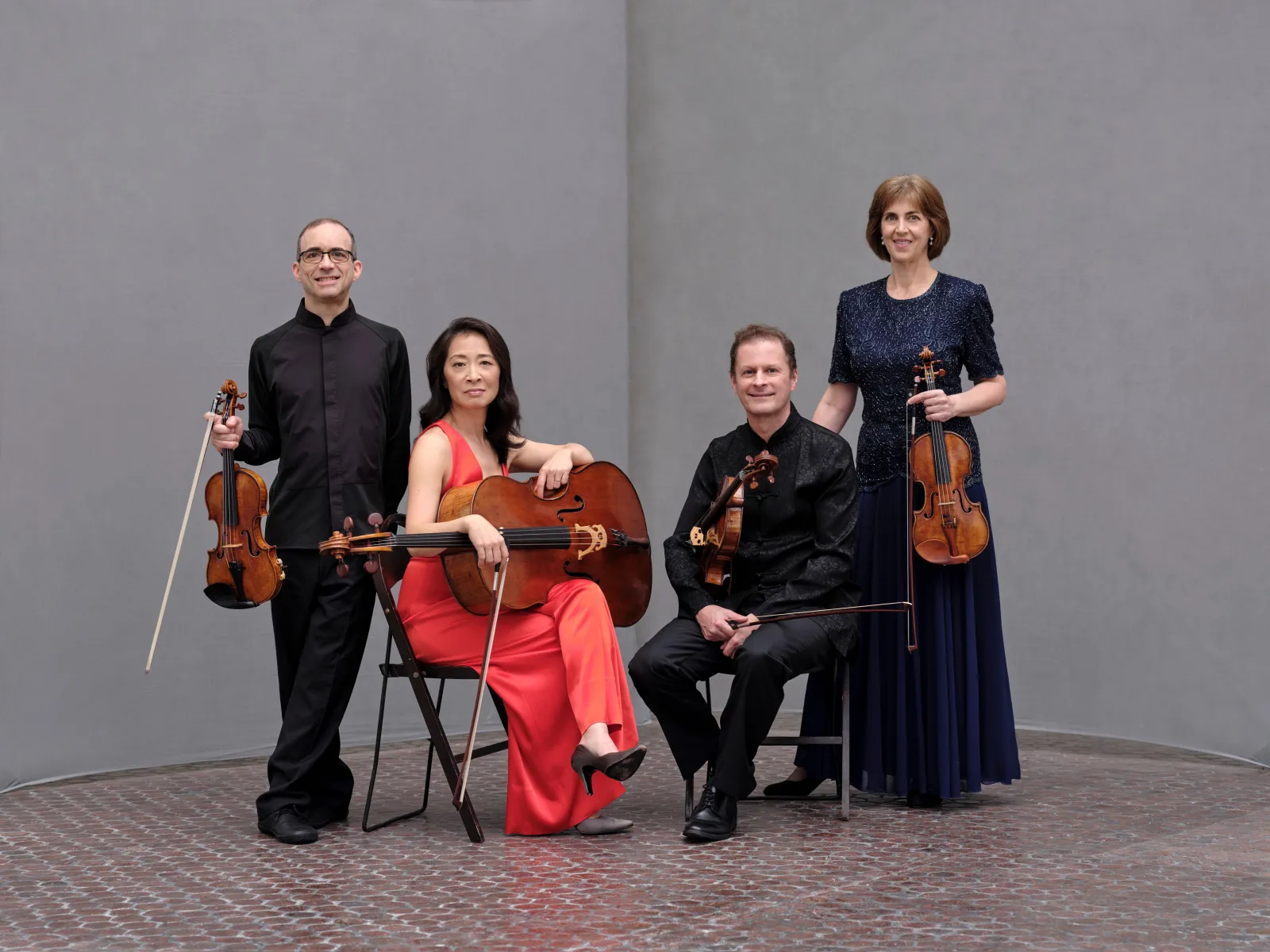 Four musicians posing together with their instruments in front of a blank wall