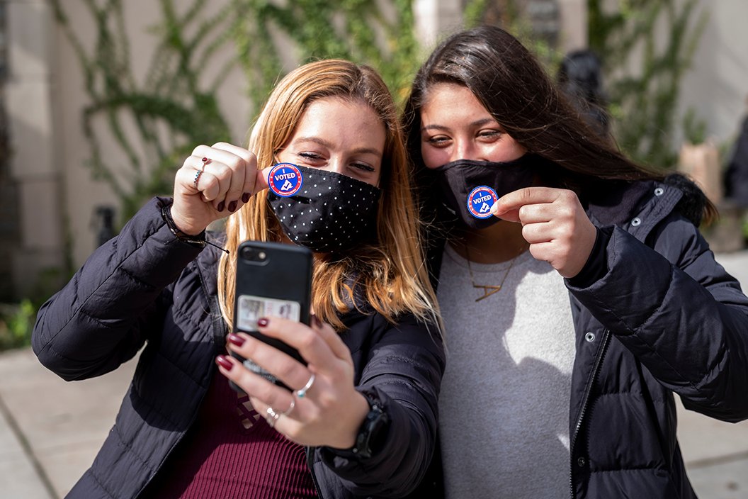 Two students wearing masks take a selfie while holding "I Voted" stickers