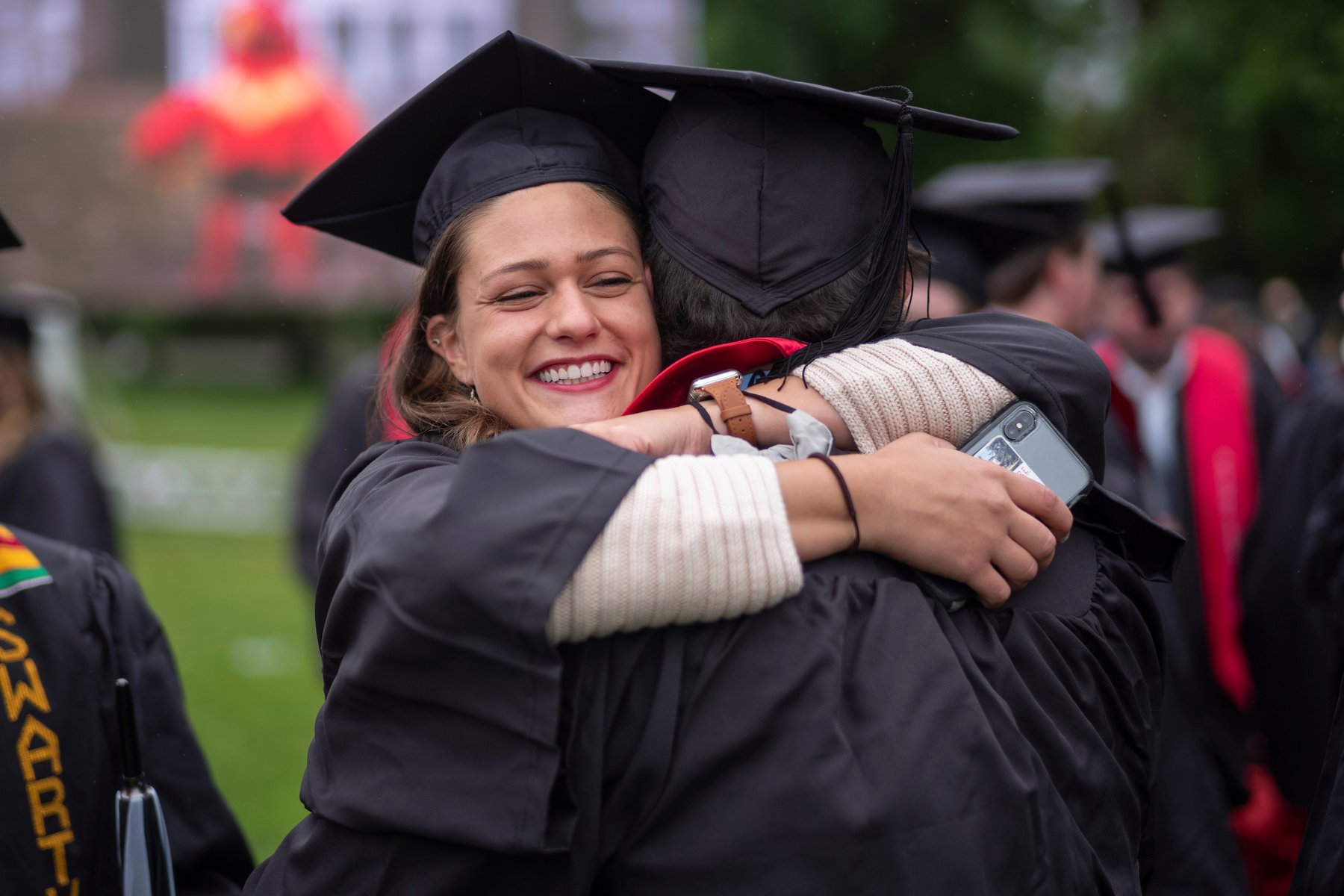 Student wearing graduation robe and cap hugs person