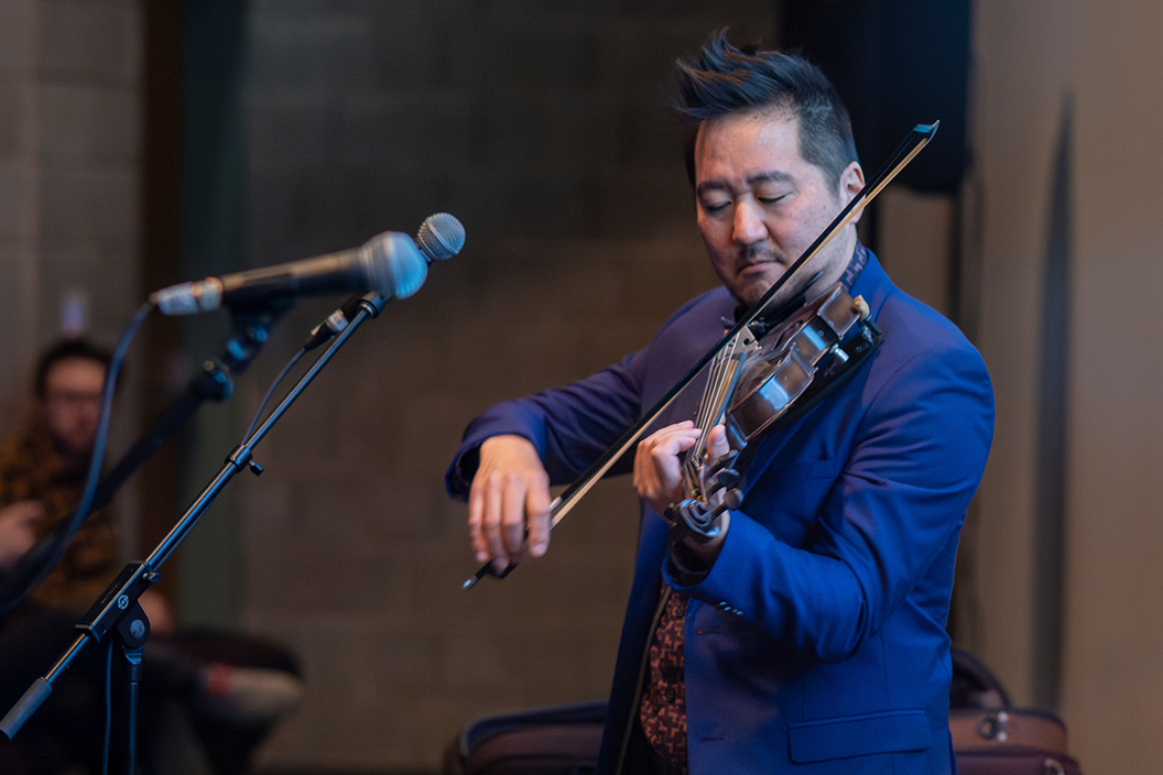 Kishi Bashi playing violin on stage into microphone