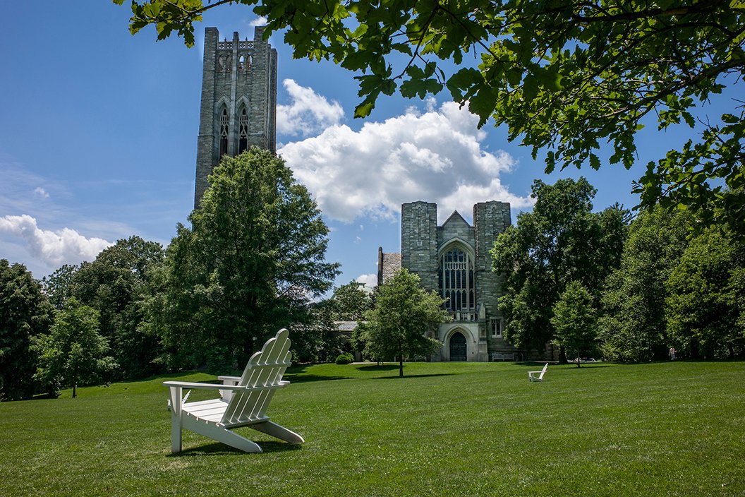 Green lawn underneath blue sky with some clouds. White Adirondack chair in foreground.