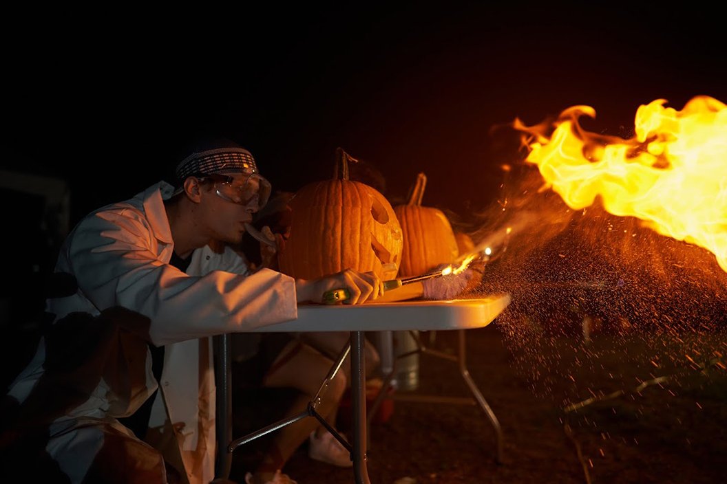 Student blows through tube into pumpkin, producing flames