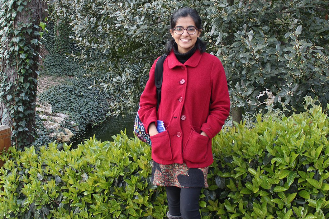 Person in red coat stands in front of green bushes