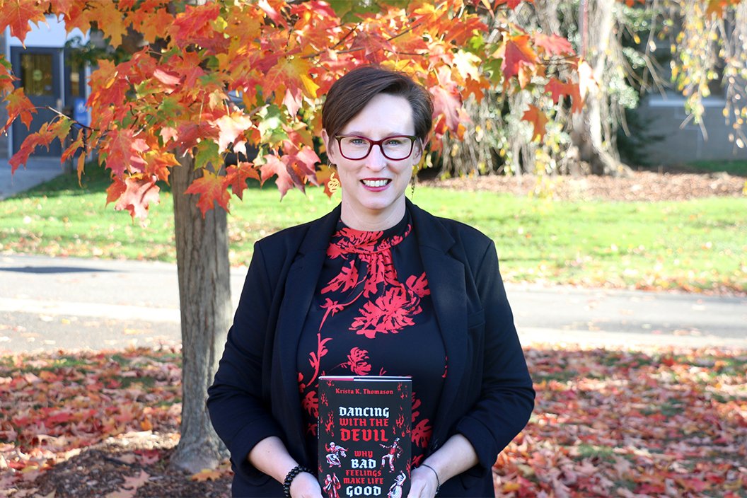 Krista Thomason poses with book in hands in front of fall foliage 