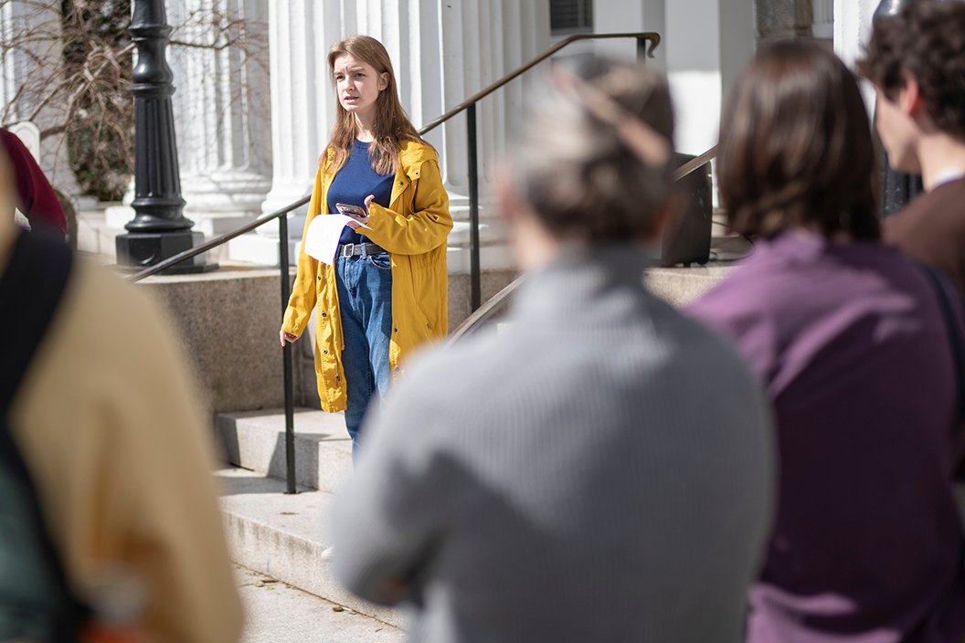 Person wearing yellow jacket speaks on steps outside building