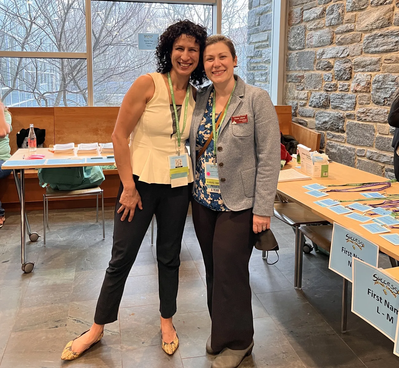 Two female professors smile in front of conference registration tables