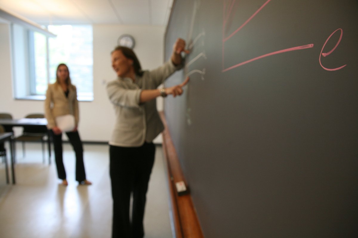 economics professor, Amanda Bayer, writing at far end of a chalkboard 
