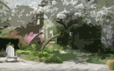 A lone adirondak chair in a beautiful garden of blooming trees