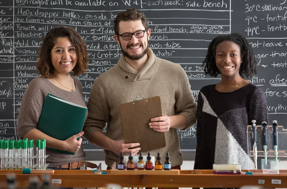 Three students face the camera in a science classroom