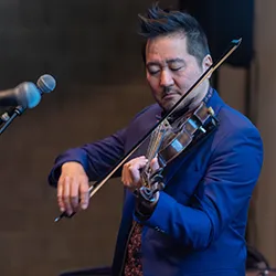 Kishi Bashi playing violin on stage into microphone