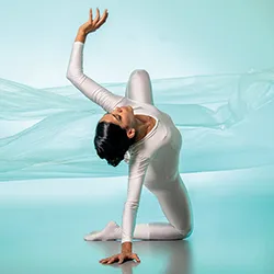 Person in white bodysuit dances on stage in front of blue-green background