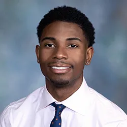 Deante Bryan '20 wearing tie, smiling against blue background