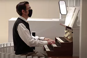 Man in mask sits at pipe organ and plays sheet music